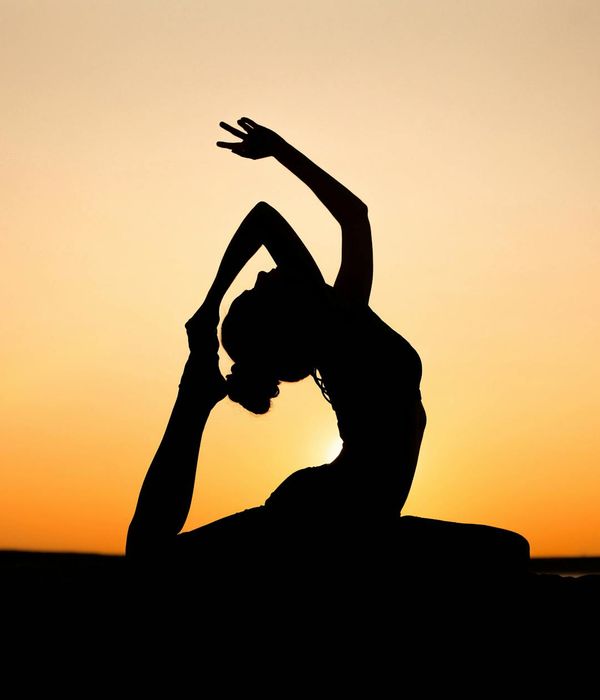 Silhouette of a person in a yoga tree pose against a beautiful sunset.
